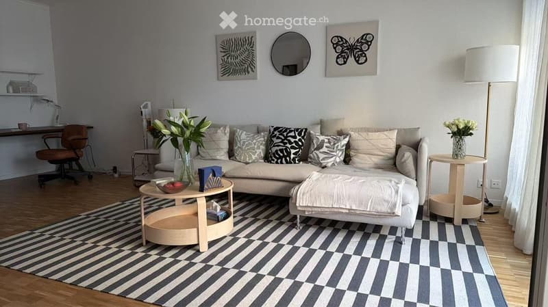 Modern living room with a light-colored sofa, ottoman, coffee table, side tables, floor lamp, and artwork on the walls.