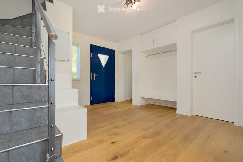 Bright hallway with wooden flooring, white walls, built-in closet, staircase leading upwards, and a blue door.
