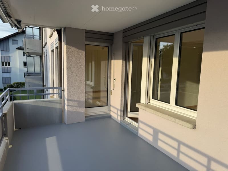 Balcony with large windows, sliding glass doors, metal railing, and a view of neighboring buildings.