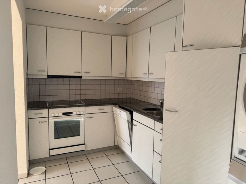Modern kitchen with light wood cabinets, tiled backsplash, and stainless steel appliances including an oven and dishwasher.