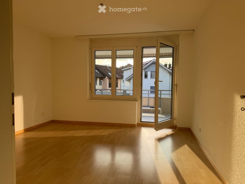 Empty room with wooden flooring, large windows, and sliding glass doors leading to a balcony.