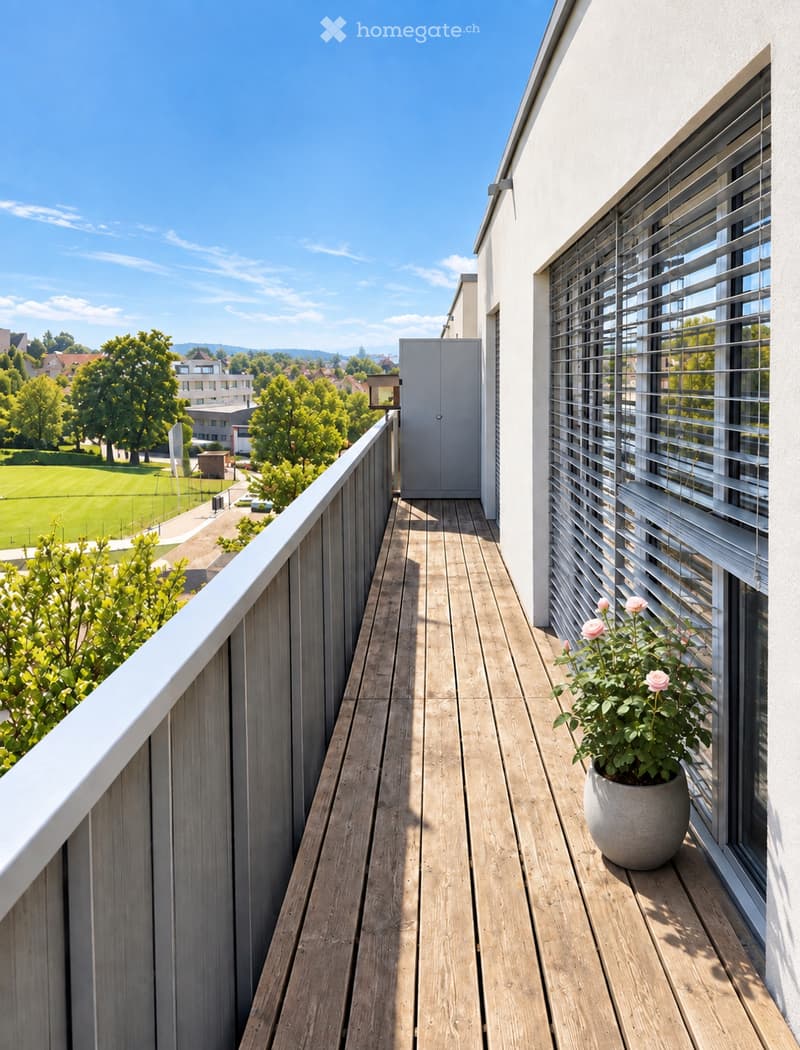 Wooden balcony with white railing, flower pot with pink flowers, and a view of a green park and buildings.