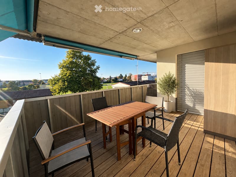 Balcony with wooden decking, outdoor table and chairs, potted plant, and a view of the surrounding area.