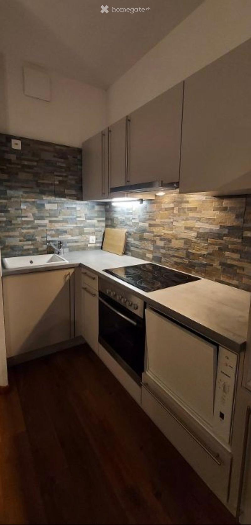 Modern kitchen with light-colored cabinets, a stone backsplash, and built-in appliances including an oven and dishwasher.