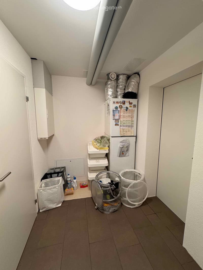 Laundry room with appliances, storage racks, garbage bins, a white refrigerator, and various items on the shelves.