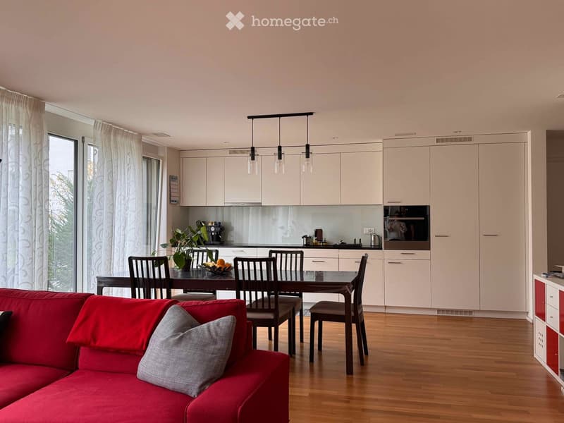 modern living room with kitchen and dining area, wooden floors, white kitchen cabinets, dark wood dining table, pendant lights, white curtains, modern red couch