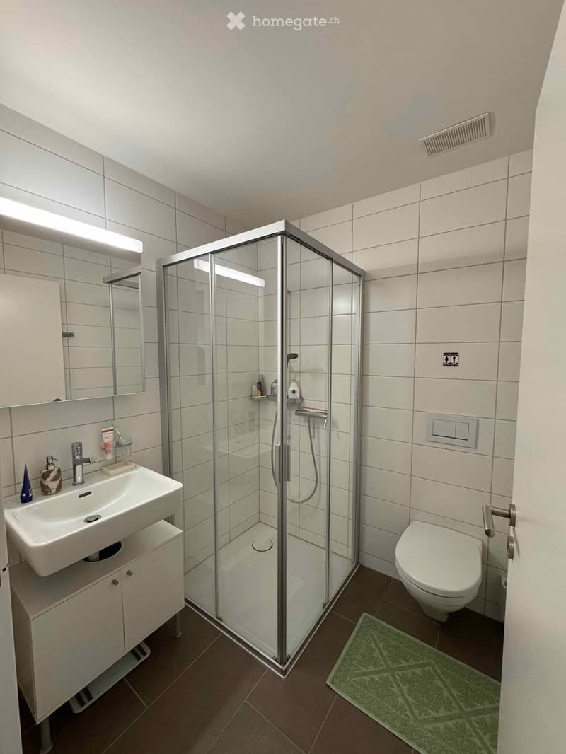 White tiles, glass shower, white sink, white cabinets, white toilet