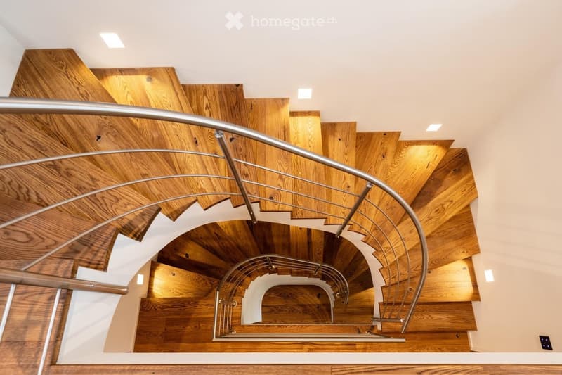 Spiral staircase with wooden steps and a modern metal railing, illuminated by recessed ceiling lights.