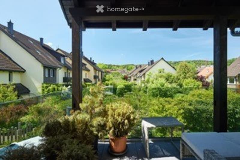Balcony with wooden decking, potted plants, small table, and view of a residential neighborhood with houses and greenery.