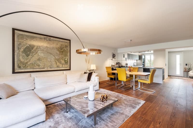 Modern open-plan living and dining area with a white sectional sofa, coffee table, dining table with yellow chairs, and a sleek kitchen area in the background.