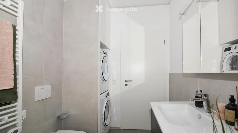 Modern bathroom with a bathtub, washing machine, towel rack, and decorative items on the sink.