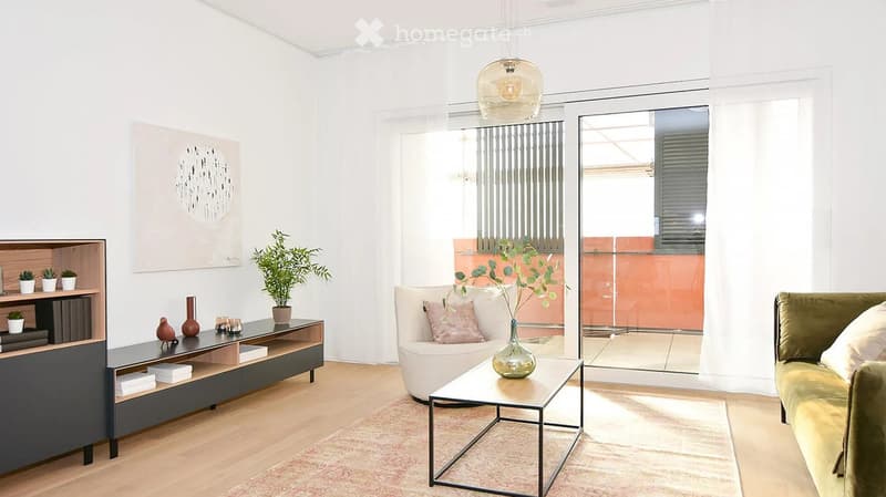 Modern living room with a green velvet sofa, white armchair, glass coffee table, and a sleek black shelf unit. Features a large sliding glass door leading to a balcony, wooden flooring, and decorative plants.