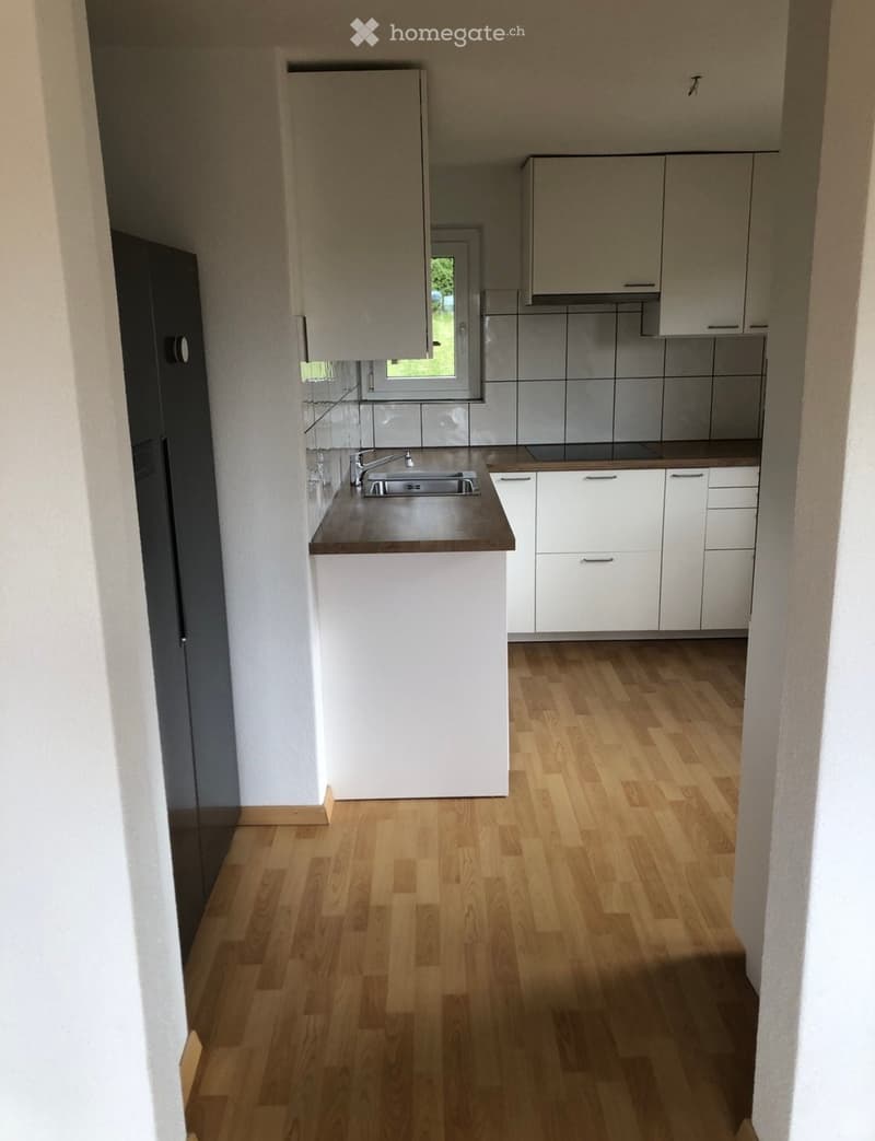 Modern kitchen with light wooden flooring, white cabinets, a sink with a faucet, and a window letting in natural light.