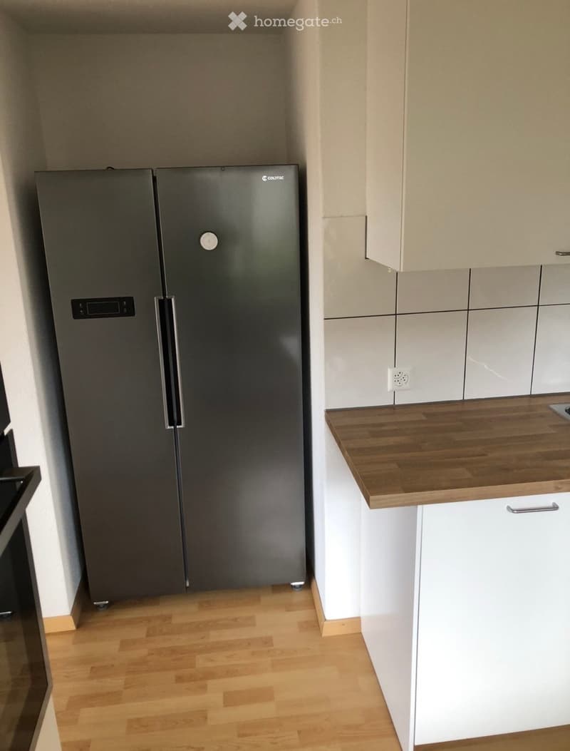 Modern kitchen with light wood flooring, white cabinets, and a stainless steel refrigerator.