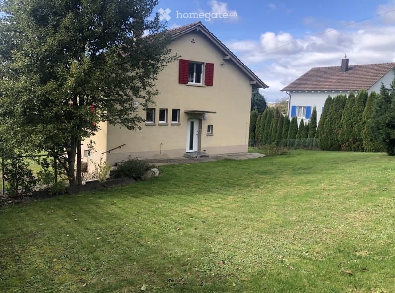 Single-story house with beige walls, red shutters, and a well-maintained lawn in front.