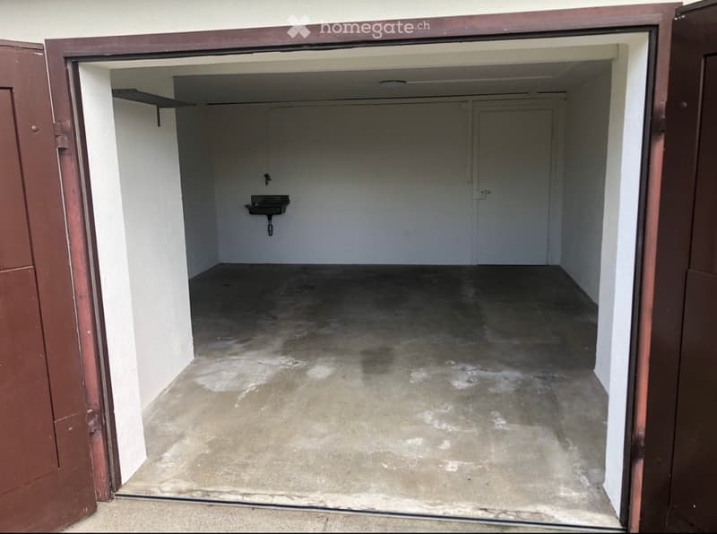 Empty garage with concrete floor, white walls, a small sink, and a closed door at the back.
