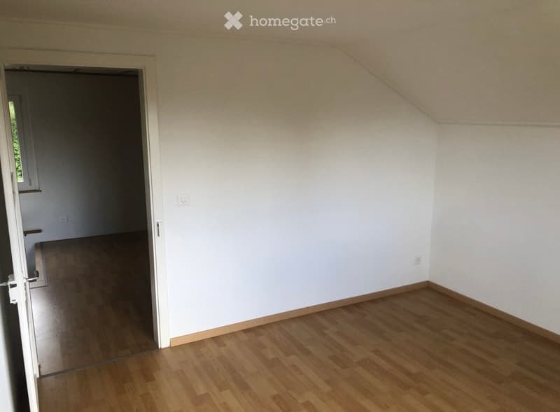 Empty room with wooden flooring and white walls, featuring a doorway leading to another room.