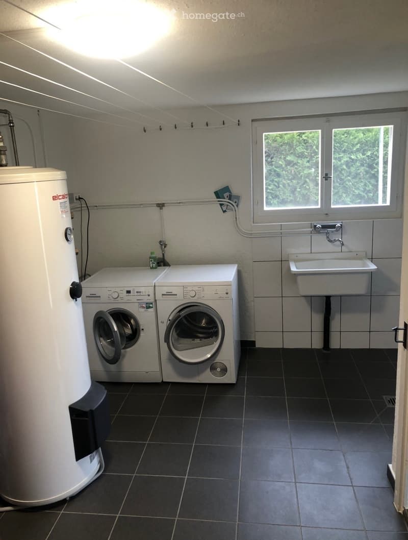 Modern bathroom with dark tiled floor, white washing machine and dishwasher, white sink, and a water heater.