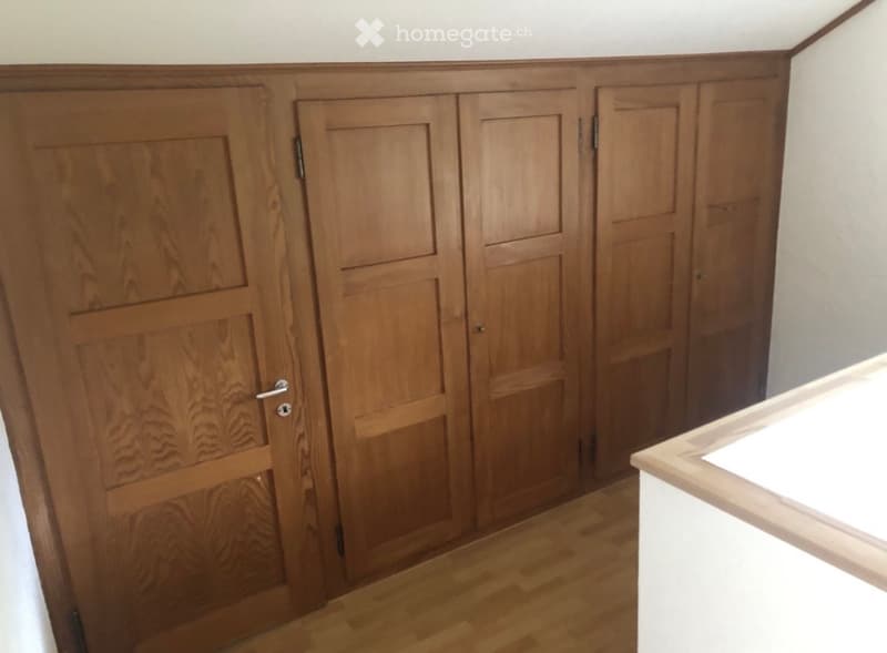 Empty hallway with wooden doors and light wooden flooring.
