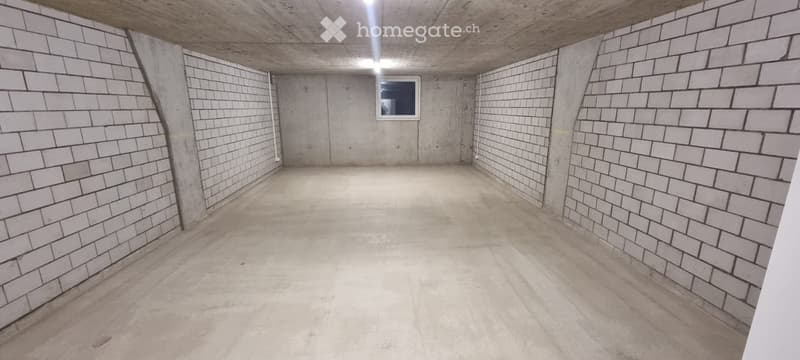 Empty underground space with concrete walls and floor, small window, and exposed ceiling beams.