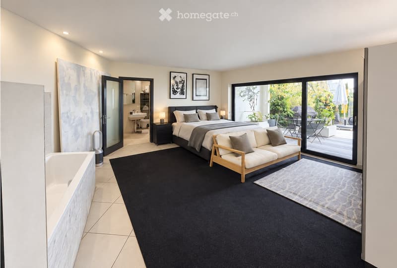 Modern bedroom with a large bed, sofa, nightstand, and a view of a garden through large sliding glass doors. The room features a black carpet, white walls, and a small bathroom area visible through an open doorway.