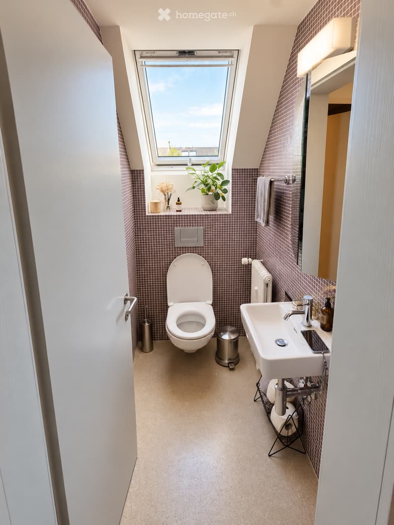 Modern bathroom with a toilet, sink, mirror, radiator, and a small window with a plant on the sill.