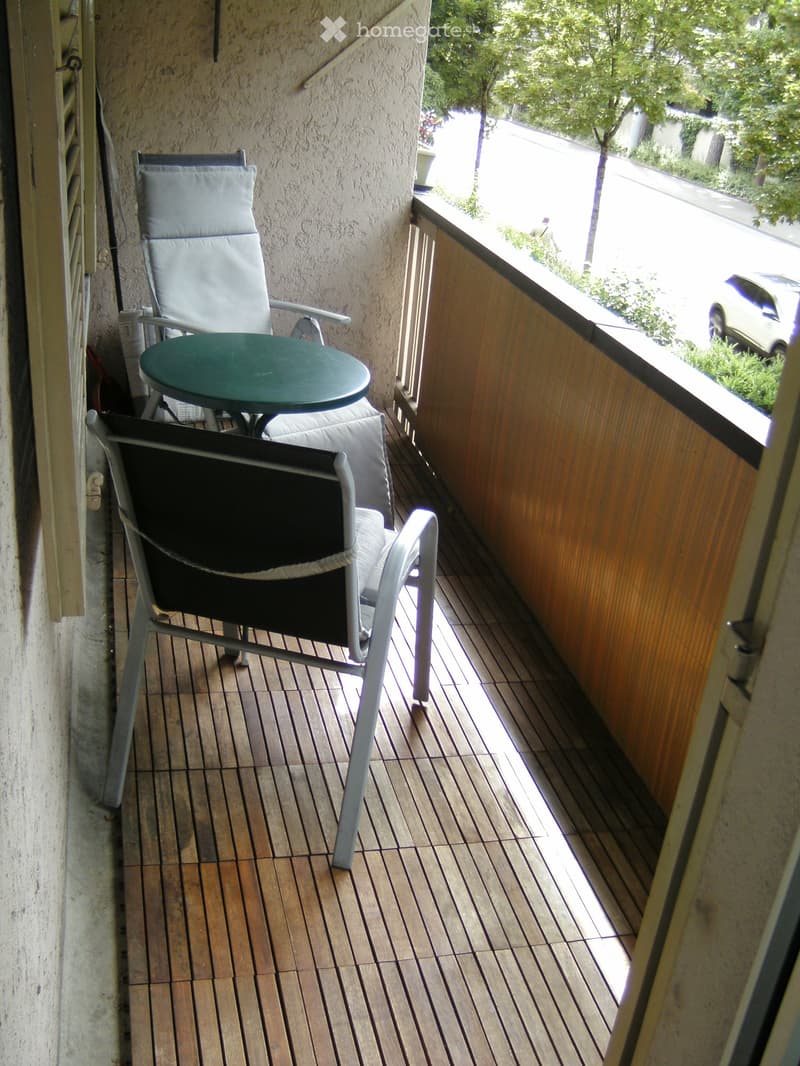 Balcony with wooden decking, two chairs, and a small round table.