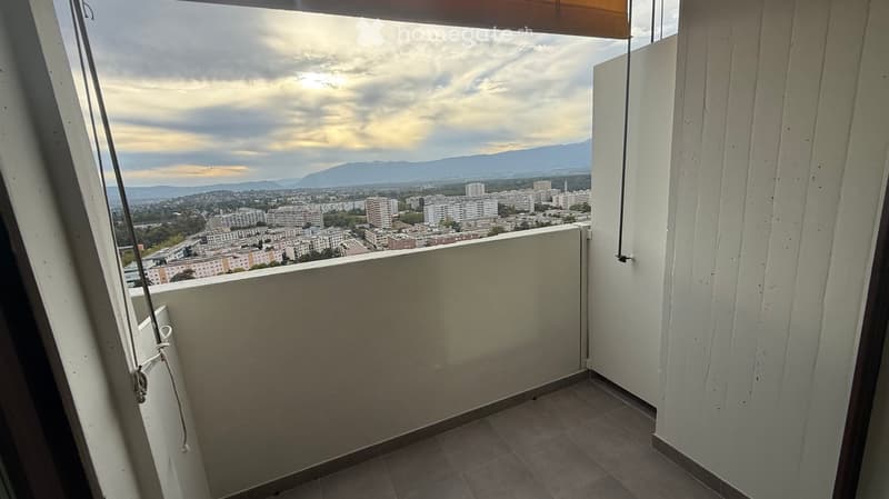 Balcony with tiled floor, white walls, and a view of a cityscape and mountains under a partly cloudy sky.