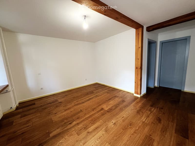 Empty room with wooden flooring, white walls, and exposed wooden beams on the ceiling. Two doors are visible on the right side.