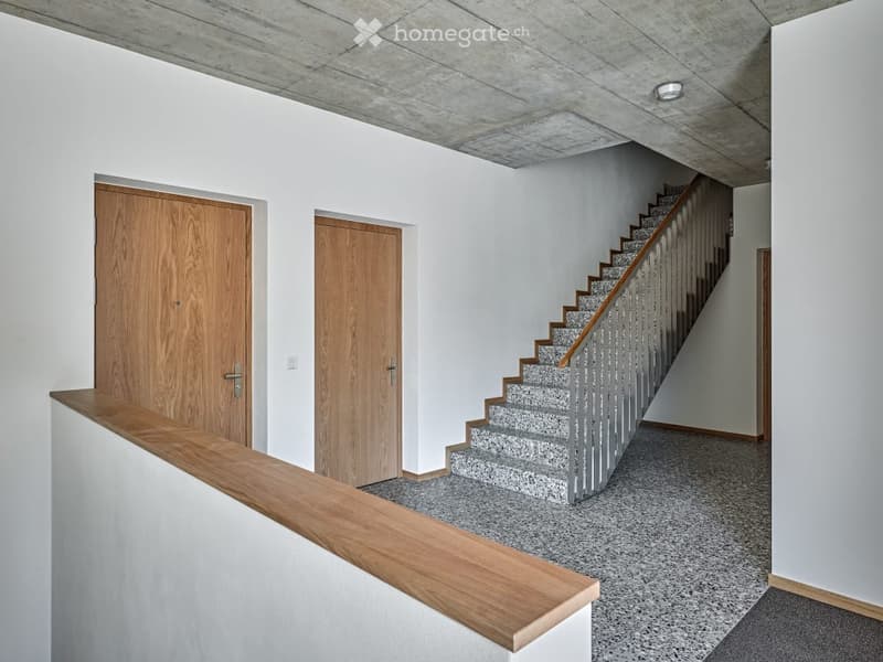 Modern hallway with a staircase leading upwards, wooden doors on either side, and a wooden railing on the landing.