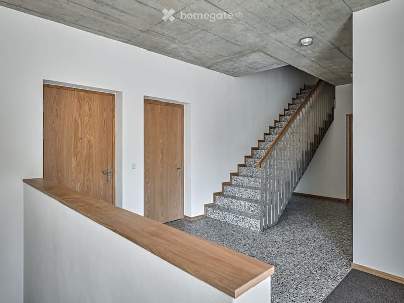 white walls, concrete ceiling, wooden handrail, gray speckled staircase, white trim around doors