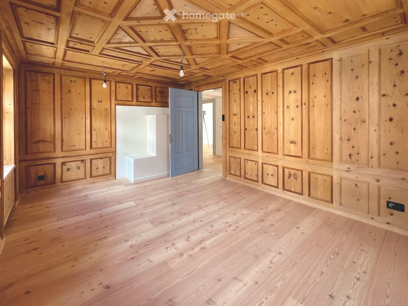 Empty room with wooden walls, wooden ceiling, and wooden floor. Features built-in wooden cabinets and a blue door leading to another room.