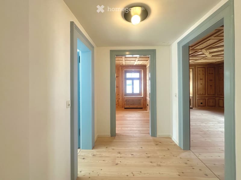 Empty hallway with wooden flooring, light-colored walls, and several open doors leading to other rooms.