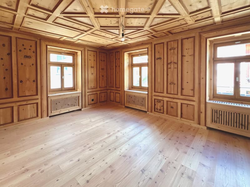 Empty room with wooden walls, ceiling, and floor, large windows, radiators, and exposed wooden beams.