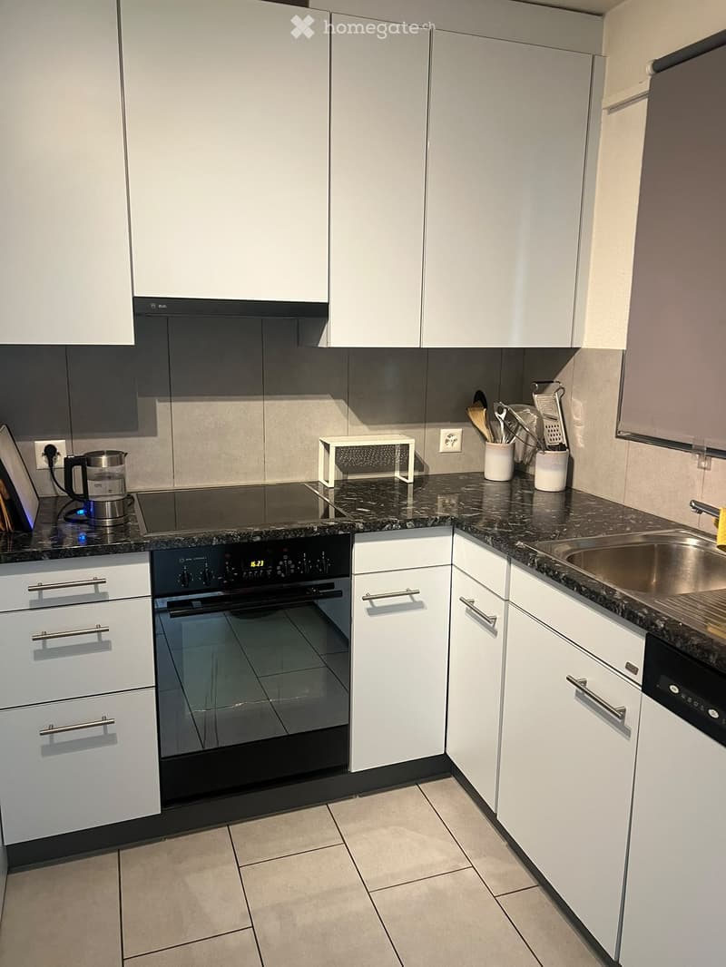 Modern kitchen with white cabinets, granite countertops, stainless steel sink, built-in oven, and various appliances and utensils.