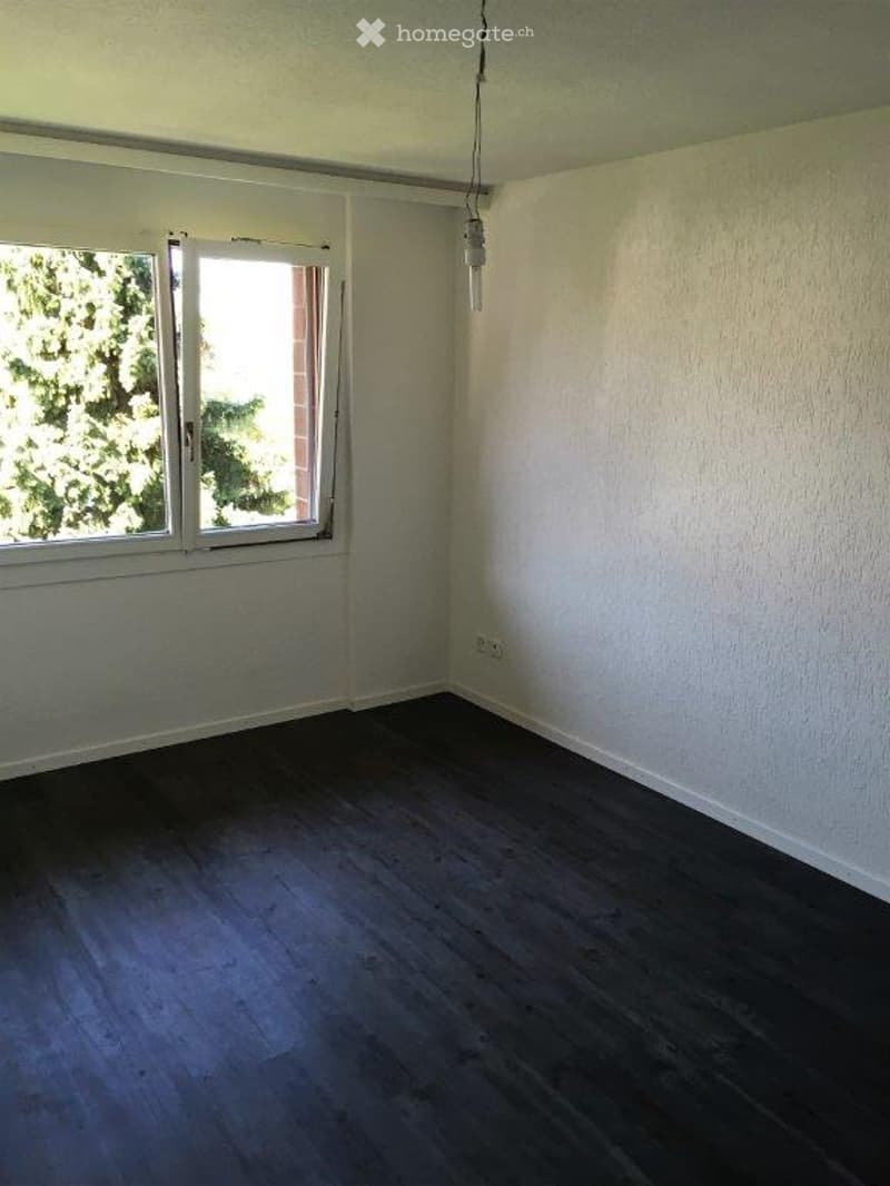 Empty room with wooden flooring, white walls, and a window with white frames. No furniture or equipment present.