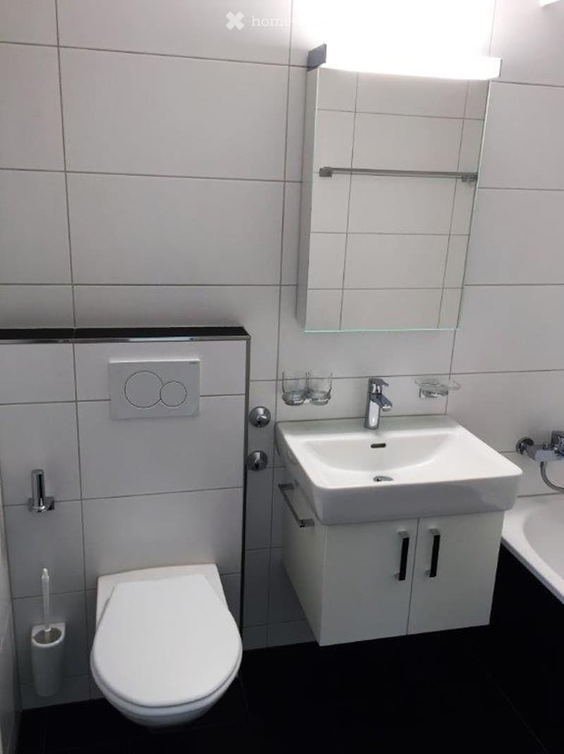 Modern bathroom with white tiles, a toilet, a sink with a mirror, and a toothbrush holder.