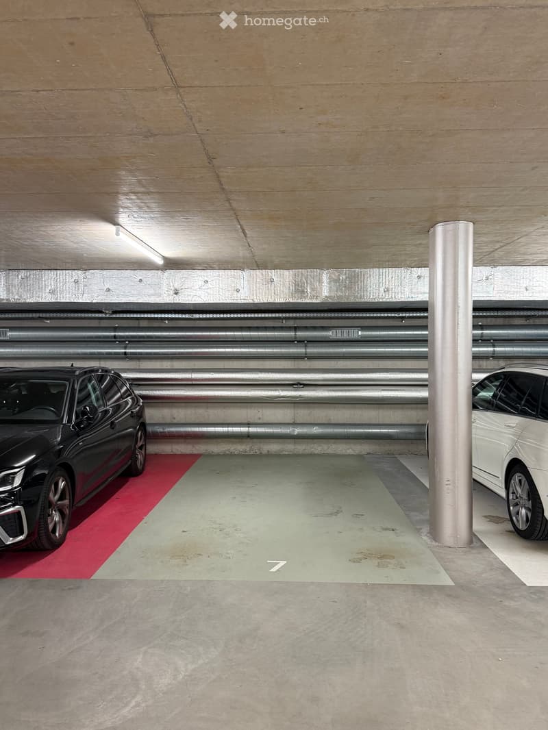 Underground parking area with two parked cars, marked parking spaces, and structural pillars.