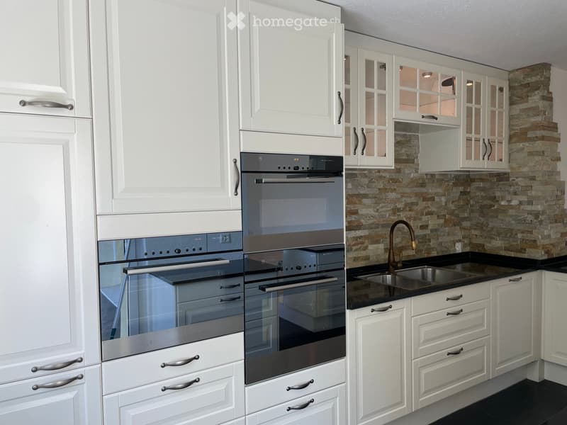 Modern kitchen with white cabinets, stainless steel oven, black countertop, and a stone backsplash.