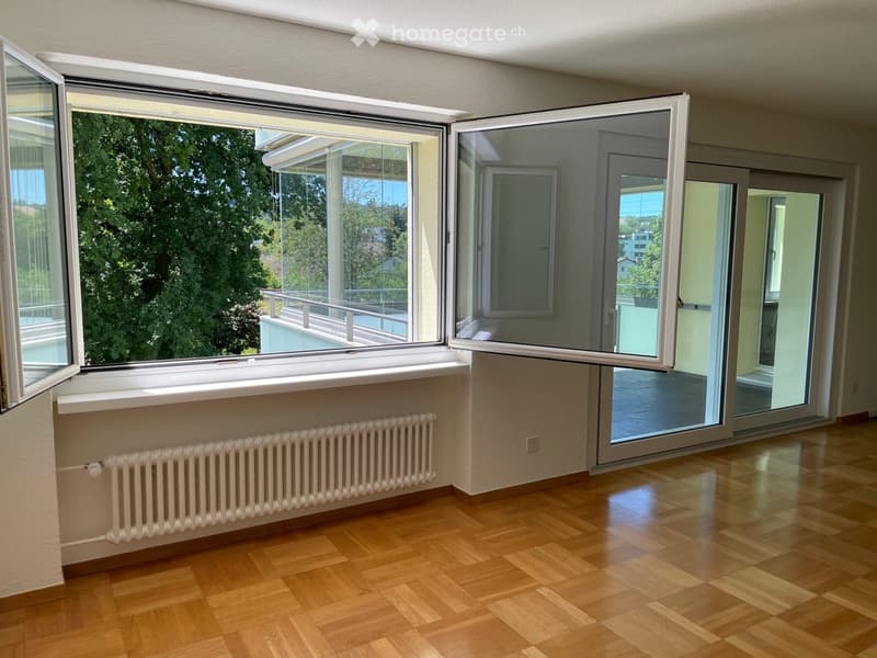 Empty room with wooden flooring, large windows with sliding doors, radiator, and a view of greenery outside.