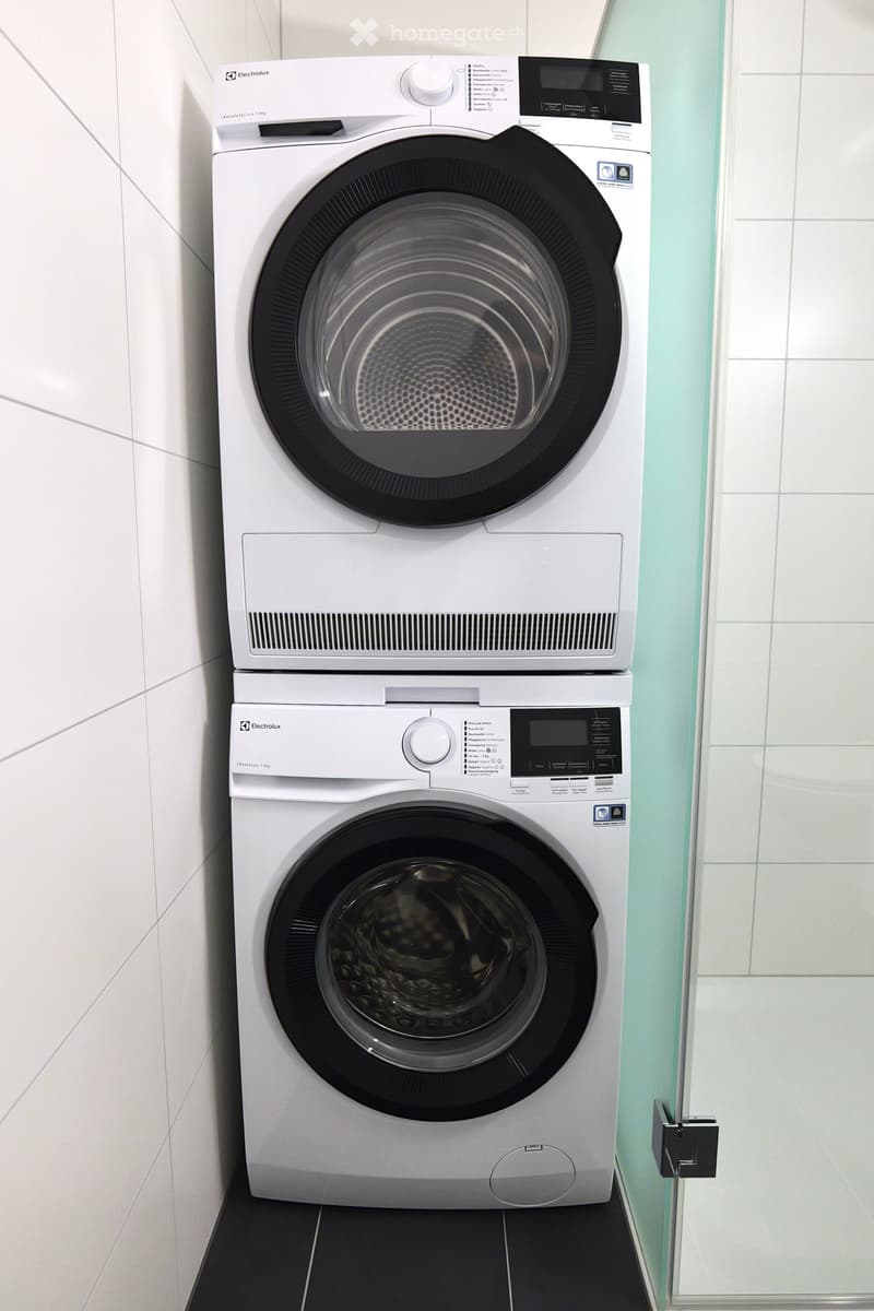 White washing machine and dryer stacked vertically in a tiled bathroom.