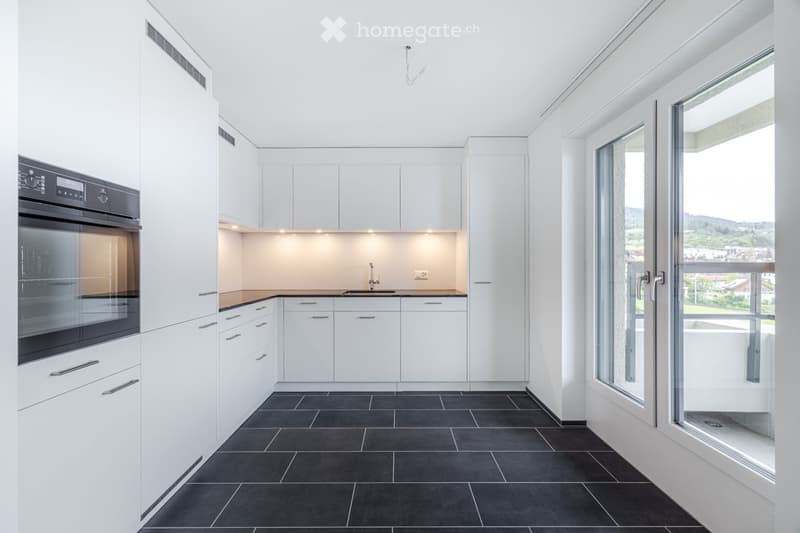Modern kitchen with white cabinets, black tiles, and large windows offering a scenic view.