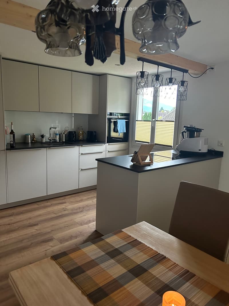 Modern kitchen with white cabinets, wooden floor, island, and various appliances. Features a dining area with a table and chair.