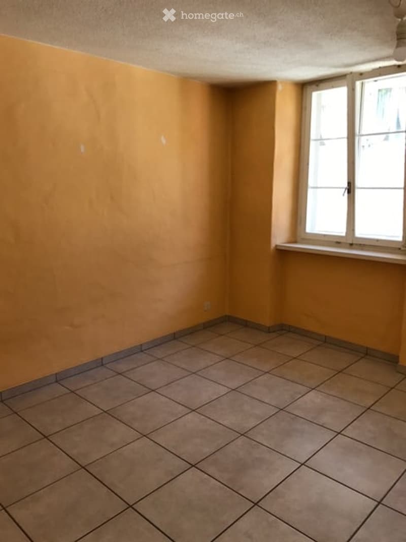 Empty room with beige tiled flooring and light yellow walls, featuring a single window with a white sill.