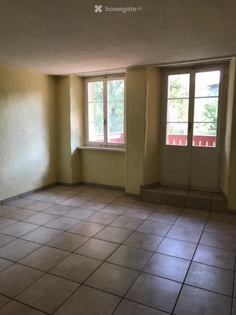 Empty room with tiled floor, two windows, and a small step leading to an outdoor area.