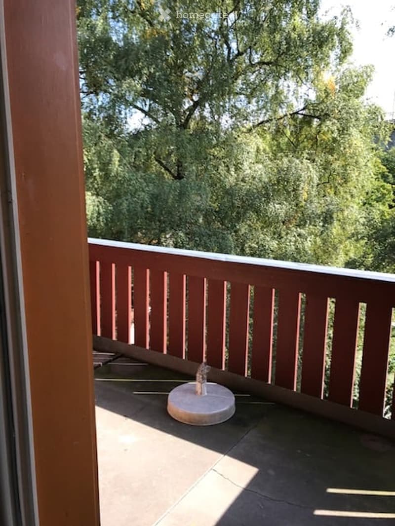 Balcony with wooden railing, tiled floor, and a small decorative item on a stand.