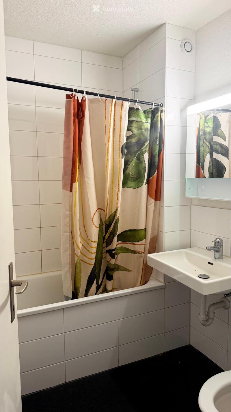 Modern bathroom with white tiled walls, black floor, bathtub, sink, mirror, and a decorative shower curtain with leaf patterns.