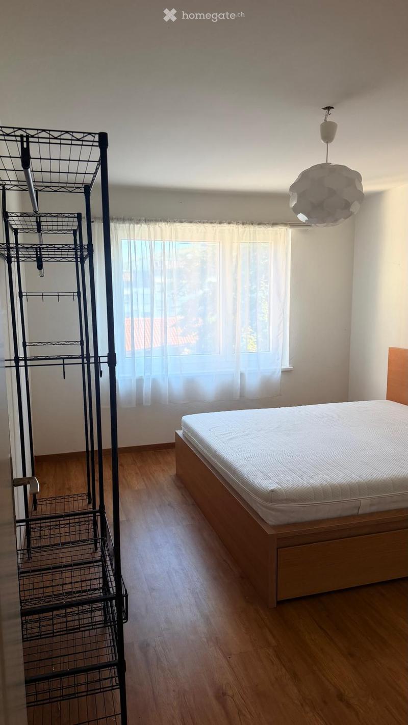 A tidy bedroom with a wooden bed frame, a mattress, a hanging rack, and a modern pendant light fixture.