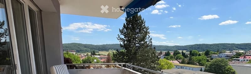 Balcony with a scenic view of a town and surrounding hills, featuring a single chair and a railing.