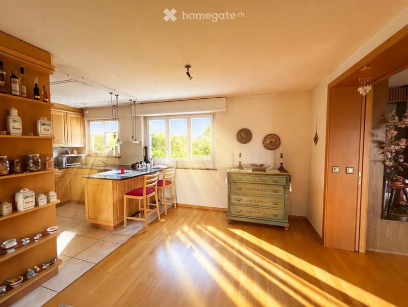 Bright kitchen with wooden floors, light-colored cabinets, a central island with bar stools, and various decorative items on shelves and surfaces.
